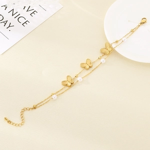 Detail of double-layer gold chain bracelet with butterflies and pearls on a white plate