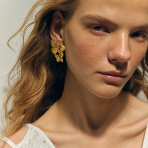 Exaggerated golden butterfly earrings in a layered artistic design on female model