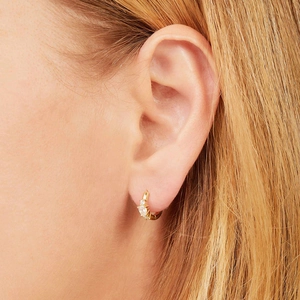 Close-up of gold huggie earrings with three sparkling zircons on female ear