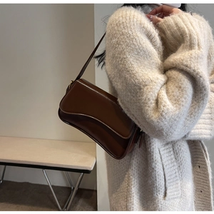 Close-up of brown glossy leather underarm bag on model in beige knitted sweater