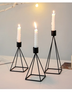 Three matte black geometric pyramid candle holders with lit white spiral candles