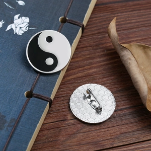 Detailed front and back view of Yin Yang Tai Chi lapel pin on a vintage book