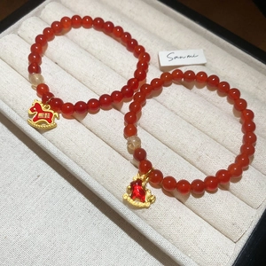 Détail macro d'un bracelet en perles d'agate rouge avec breloque cheval doré en écrin