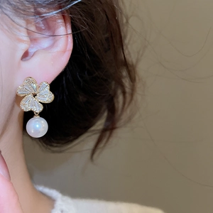 Detail of floral pearl earrings with zircon inlay worn by model in soft warm lighting