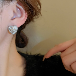 Close-up of heart-shaped zircon earrings with cross detail worn on a female ear