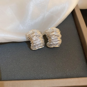 Detail shot of silver pleated hoop earrings with glossy texture on white silk fabric