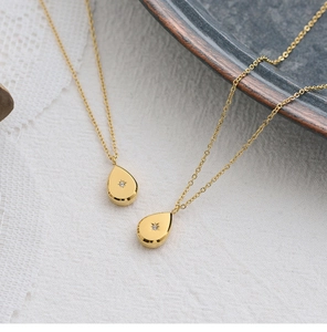 Detail view of 18K gold plated teardrop starburst necklaces on white lace background