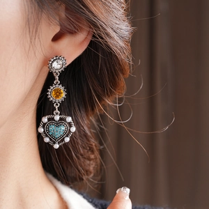 Close-up of vintage heart pendant earrings with blue crystals and pearls on a model