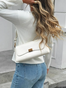 Close-up of white leather shoulder bag with gold ring detail on casual outdoor model