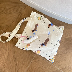 Close-up of canvas tote bag featuring cartoon dachshund prints and a white plush dog charm