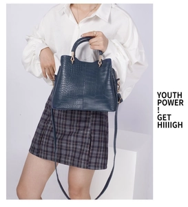 Model holding a dark blue crocodile-pattern handbag with elegant metal buckles