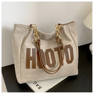 Close-up of a beige suede tote bag with brown HOOTO leather patch and metal chain strap