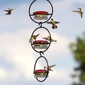 Three-tier hanging hummingbird feeder with red lids and clear bowls in natural outdoor setting