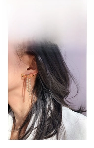 Close-up of golden bow earrings with sparkling rhinestone tassels worn by a model