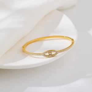 Macro shot of gold evil eye bangle with sparkling white cubic zirconia on white silk cloth
