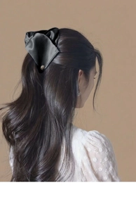 Détail d'une grande pince à cheveux en satin noir avec nœud portée sur de longs cheveux