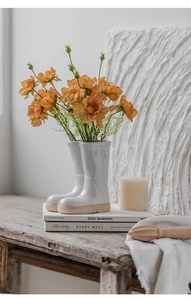 Creative white ceramic rain boot vase with orange flowers on a rustic wooden desk