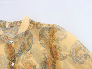 Detail of yellow paisley organza shirt featuring a round neckline and white button
