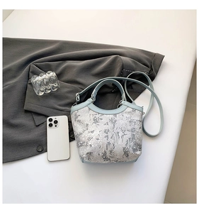 Top view of light blue bucket bag with intricate grey embroidery and a mobile phone