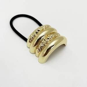 Minimalist golden shell-style elastic hair tie with textured alloy detail on cream background