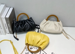 Detailed view of three pleated cloud bags in black, white, and yellow with wood handles