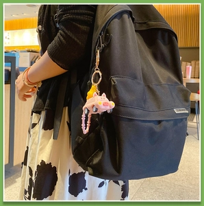 Pink cartoon pig car keychain attached to a black backpack in a cozy cafe setting