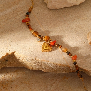 Close-up of bohemian gemstone necklace with gold heart pendant on natural rock surface