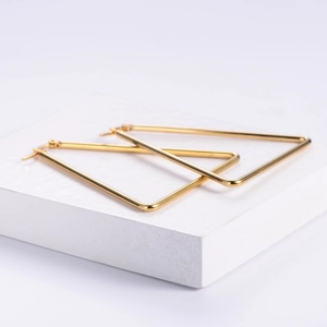 Polished gold triangle hoop earrings in geometric style displayed on a white stand