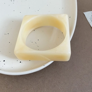 Detail view of square acrylic bangle with cream marble texture on ceramic plate