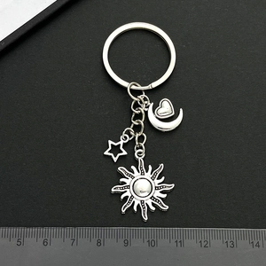 Silver metal keychain with sun, moon, star, and heart charms shown over a measuring ruler