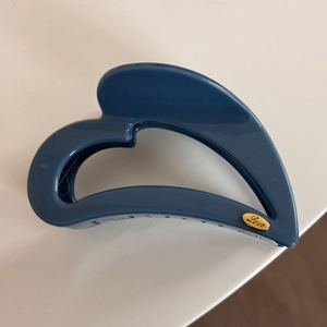 Close-up of blue hollow heart-shaped hair claw with gold Love plate detail