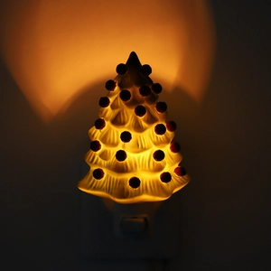 Close-up of white ceramic Christmas tree night light with red dots and warm glow