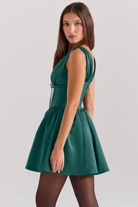 Detail of dark green sleeveless corset dress with V-neckline and pleated satin hemline