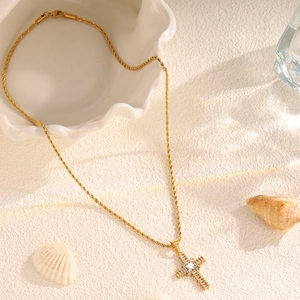 Macro shot of gold cross necklace with clear rhinestones on a white textured background