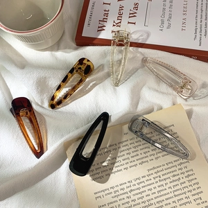 Flat lay of six diverse acrylic hair clips on textured fabric with elegant lifestyle props