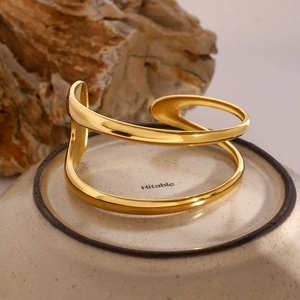 Bracelet jonc doré minimaliste à double ligne présenté sur fond de céramique et pierre