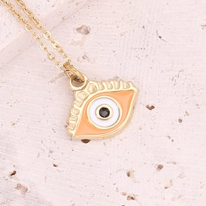 Macro detail of gold necklace with orange enamel eye pendant on a beige stone surface