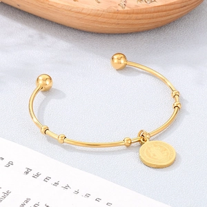 Close-up of gold plated 18K open bangle with round coin pendant and ball ends on grey background