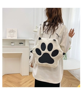 White plush cat paw backpack shown on model in a minimalist bright indoor room