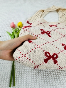 Detail of beige knitted tote bag with red bow patterns and soft textile texture