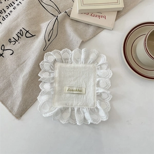 Detail of white square coaster with heart lace edge and small fabric label on white table