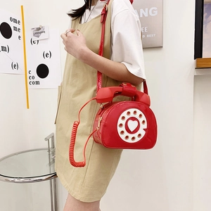 Detail of red patent leather crossbody bag in unique retro telephone design worn by model