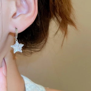 Macro side view of a model wearing sparkling star-shaped silver earrings with zircon stones