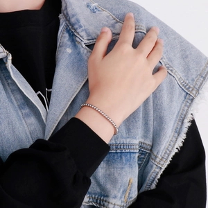 Close-up of minimalist silver stainless steel bead bracelet worn on wrist with denim jacket