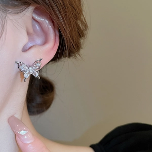 Close-up of a delicate silver butterfly stud earring with white zircons on a model's ear