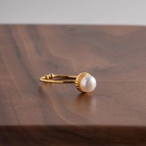 Close-up of a gold adjustable pearl ring on a dark wooden surface with warm lighting