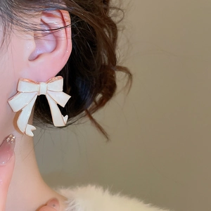 Close-up of elegant cream enamel bow stud earring worn by model in warm lighting