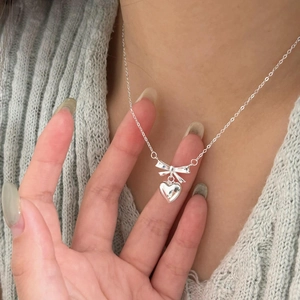 Detail of 925 sterling silver bow and heart pendant necklace on light blue knit background
