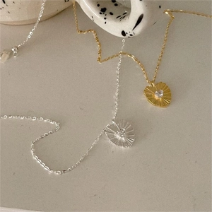 Close-up of gold and silver heart necklaces with sunray texture on a ceramic cup
