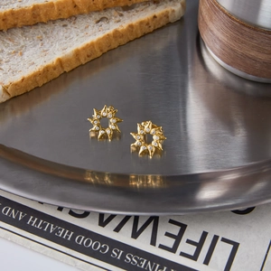 Macro detail of sunburst gold earrings with clear zircons on a rustic tabletop display